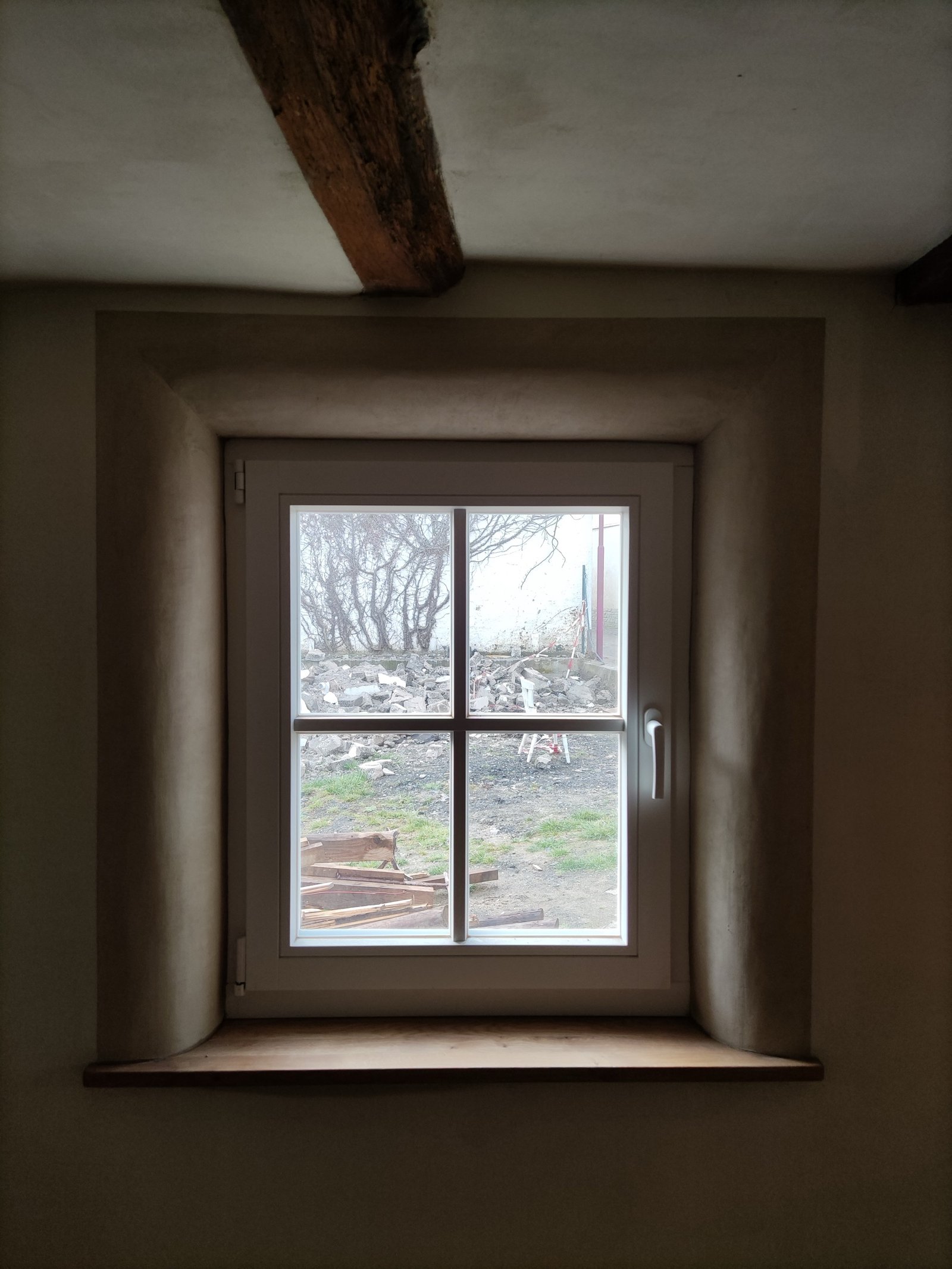 Neu eingesetztes Sprossenfenster in verputzter Fachwerkwand, dahinter Trümmergrundstück