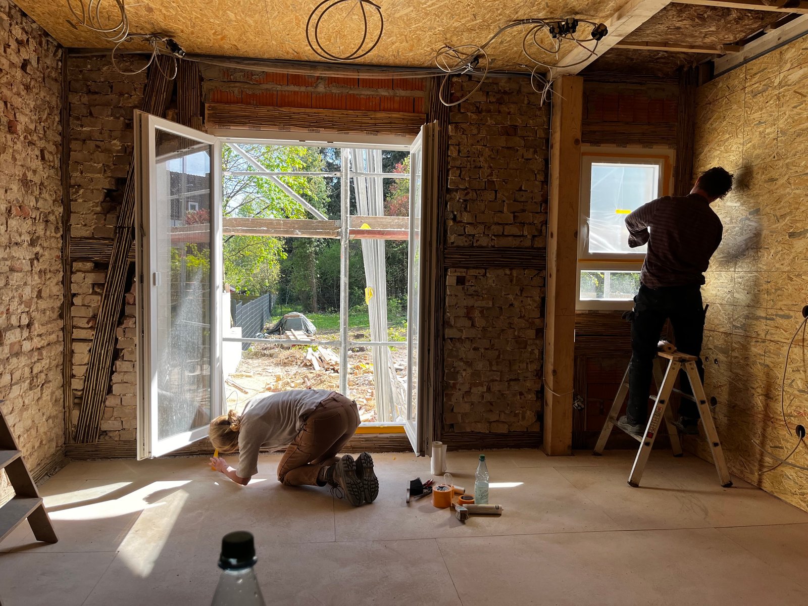 Altbau-Sanierung Kassel: Innenraum mit freigelegtem Bruchstein, zwei Handwerker bei Arbeit