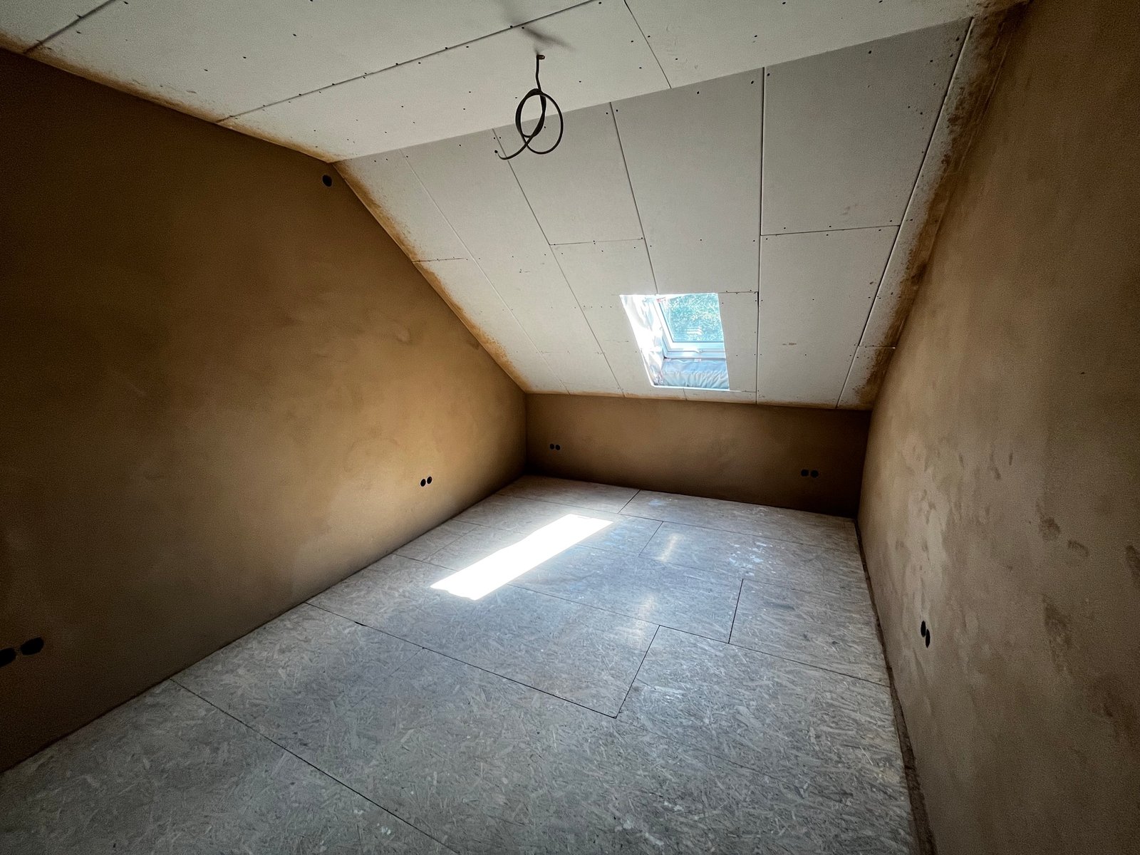 Lehmputz-Dachgeschoss: fertig verputzte Schrägwände, Dachfenster, warmer Braunton