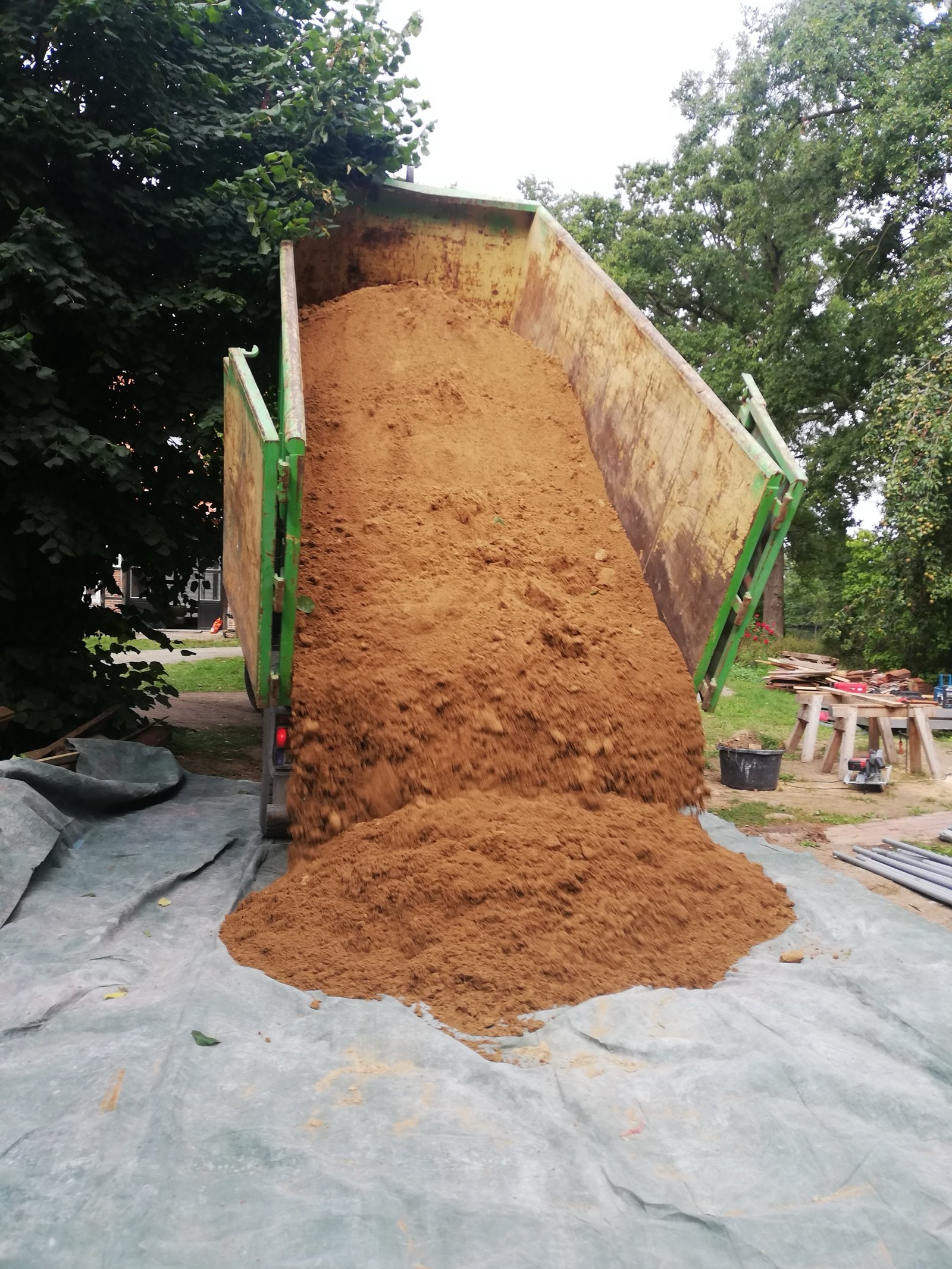 Lehmanlieferung für Künstlerhaus: Kipper entlädt roten Rohton auf Plane im Garten