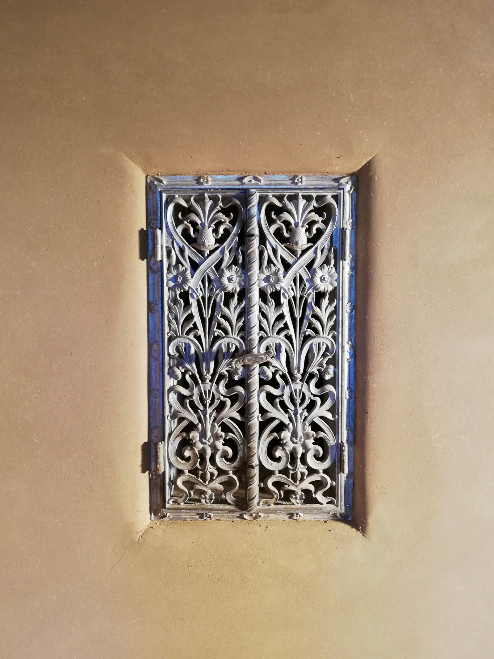 Schmiedeeisernes Fenster in Lehmputzwand: kunstvolles Gitter, Jugendstil-Ornamentik
