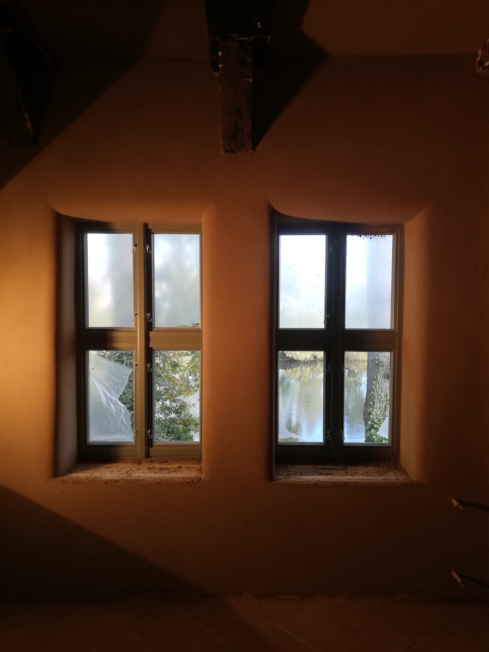 Lehmputzraum Künstlerhaus: zwei Holzsprossenfenster in fertig verputzter Wand
