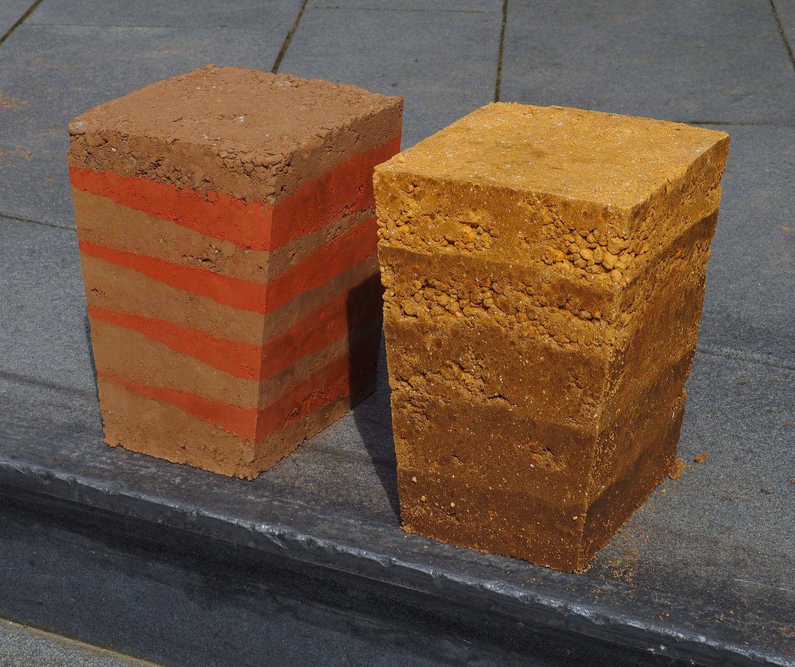 Stampflehm-Workshop: zwei Lehmziegelproben mit Schichtstruktur, rot-beige Lagen