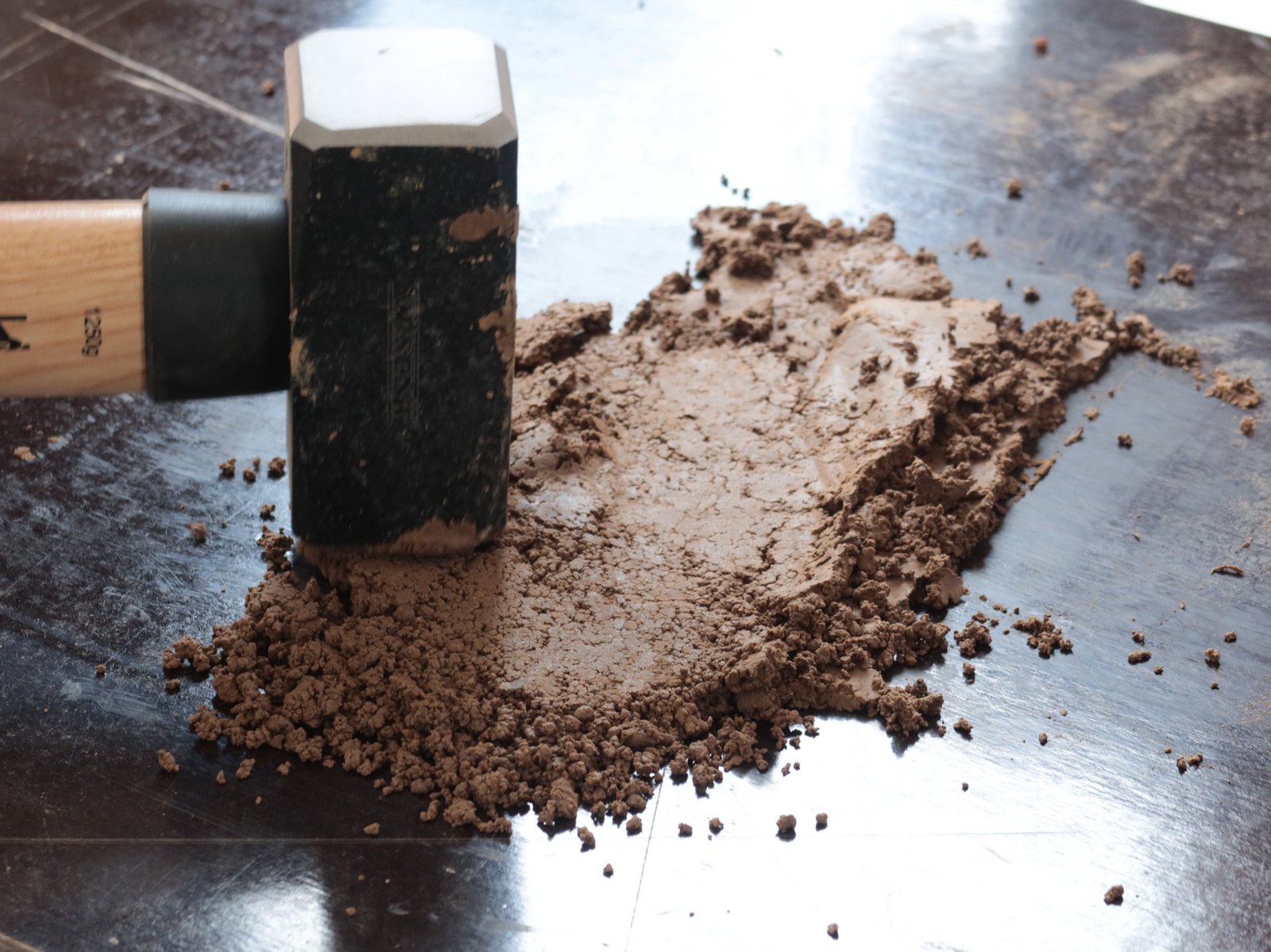 Lehmklumpen mit Hammer zerschlagen: Schlagspuren auf dunklem Untergrund