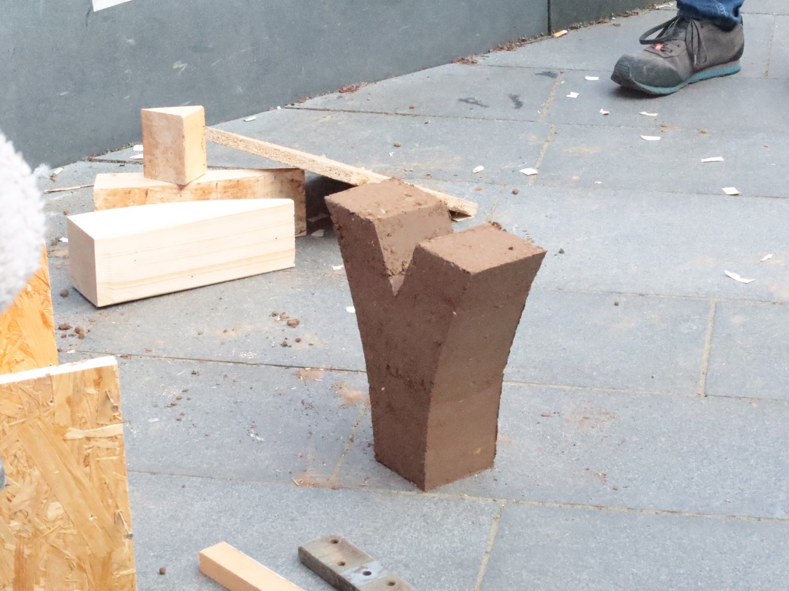 Stampflehm Y-Form: frisch entformter Lehmkörper auf Pflasterstein, Holzschalung