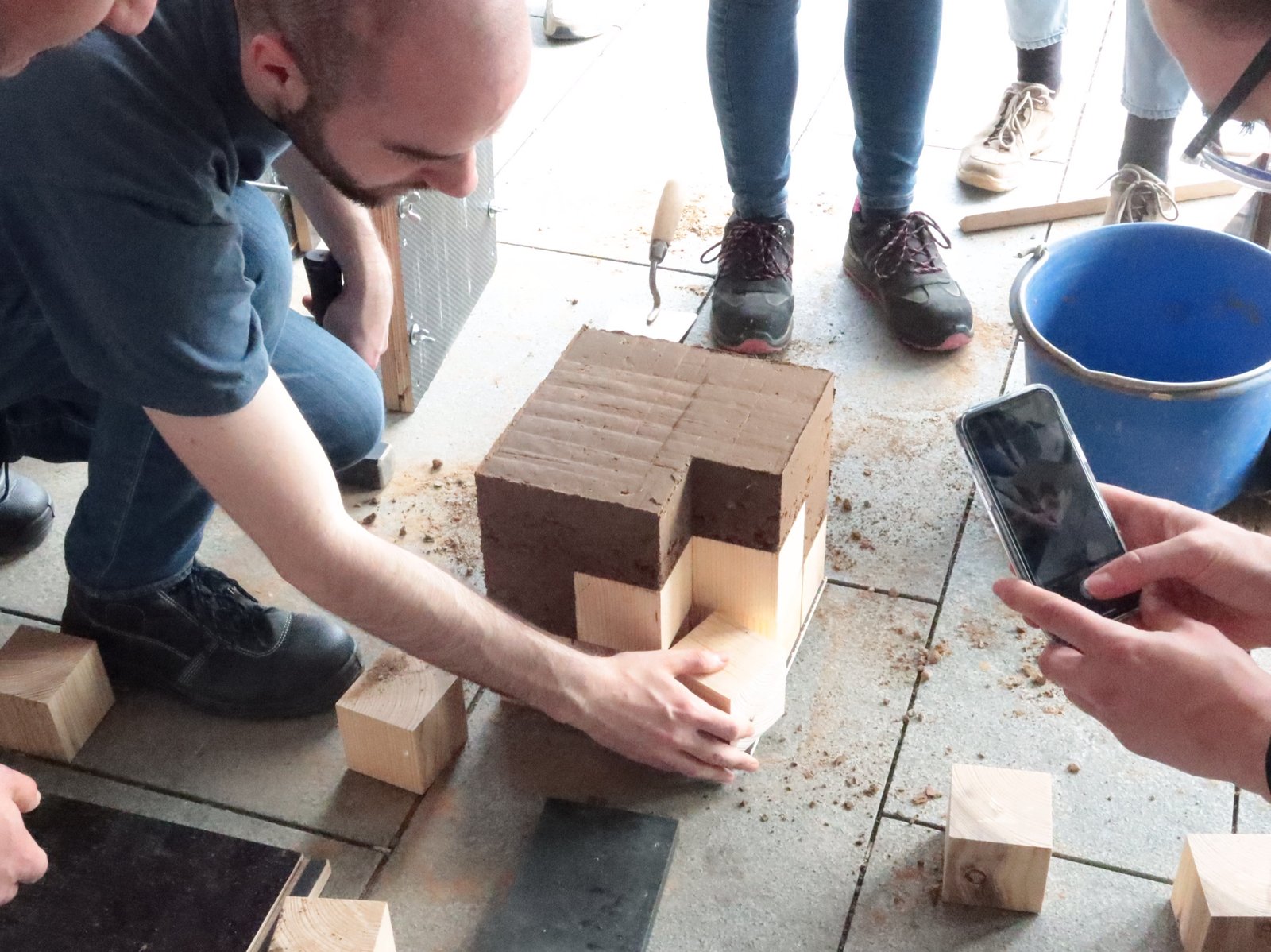 Stampflehm-Workshop: Studierender öffnet Holzschalung von gestampftem Lehmkörper