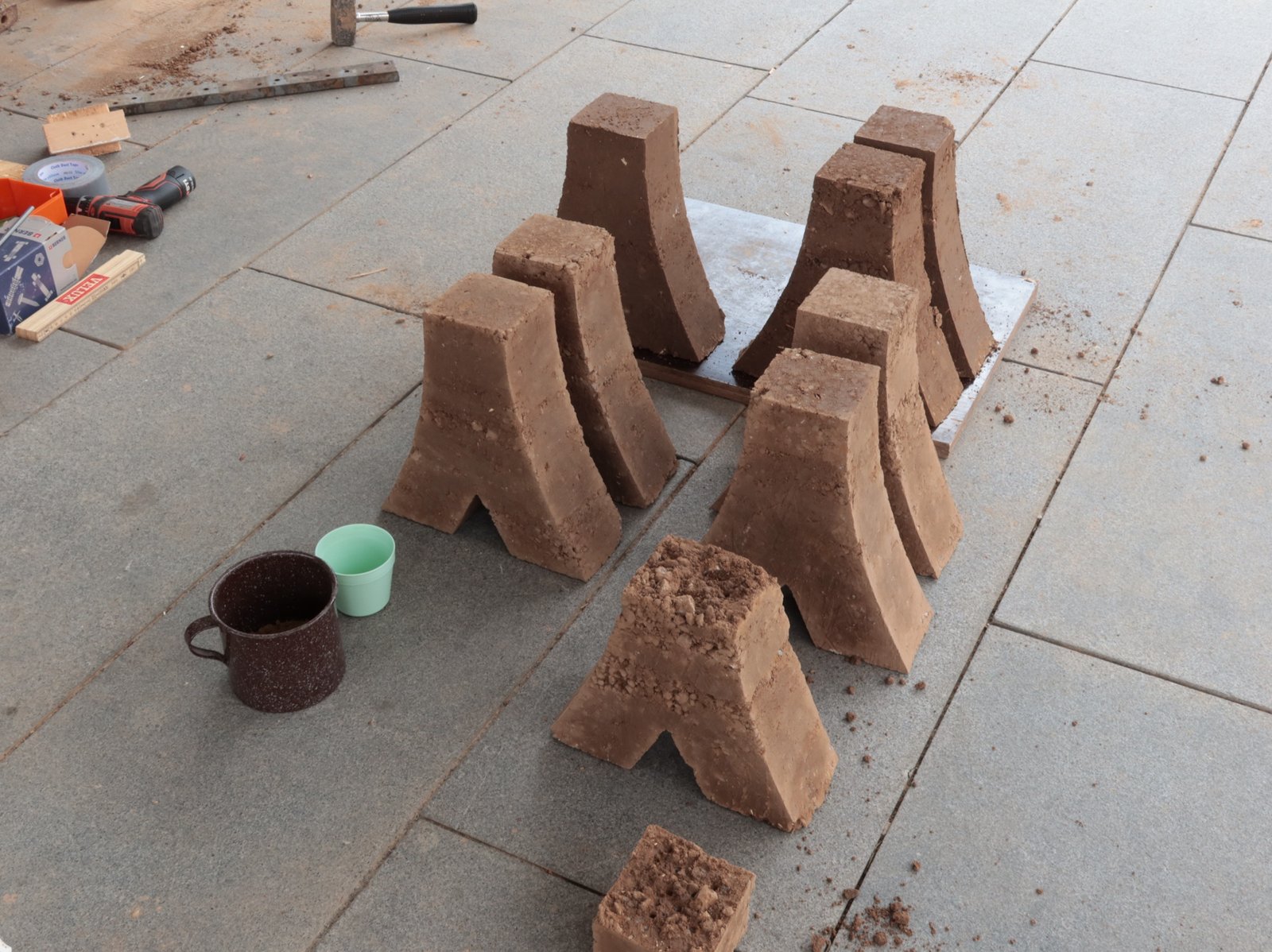 Stampflehm Y-Formen: acht entformte Lehmkörper auf Pflasterstein, Workshop