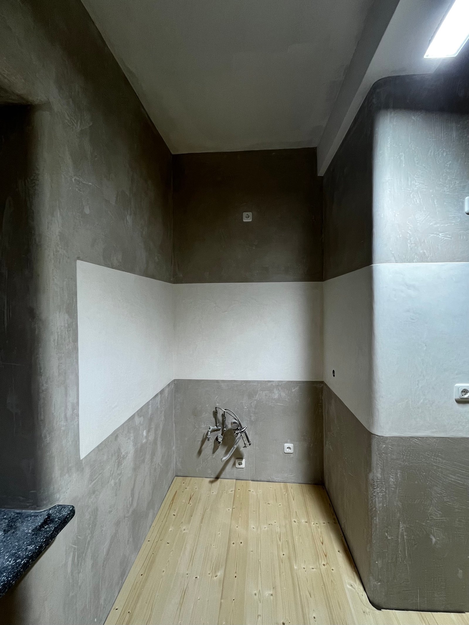 Fertig saniertes Bad mit Lehmputz: graue Tadelakt-Wände, Holzdielenboden, Wandarmatur