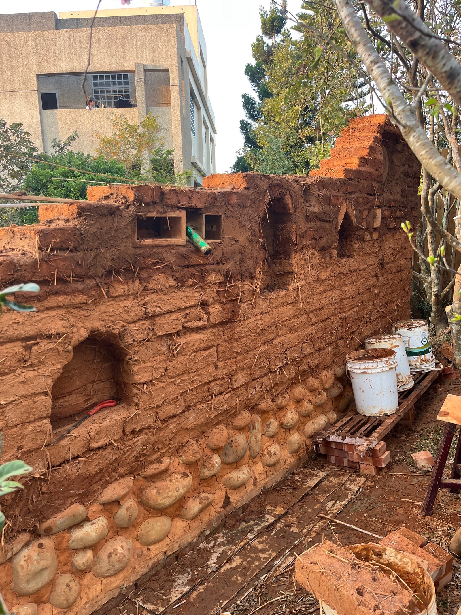 Lehmziegelmauer mit Flusssteinbesatz im Bau: Aufschichtung mit Backsteinband