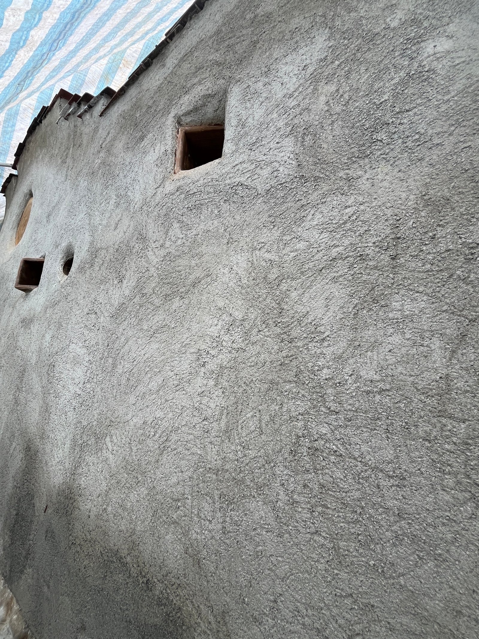 Lehmputz-Wandoberfläche grob: graue Außenwand mit zwei kleinen Öffnungen