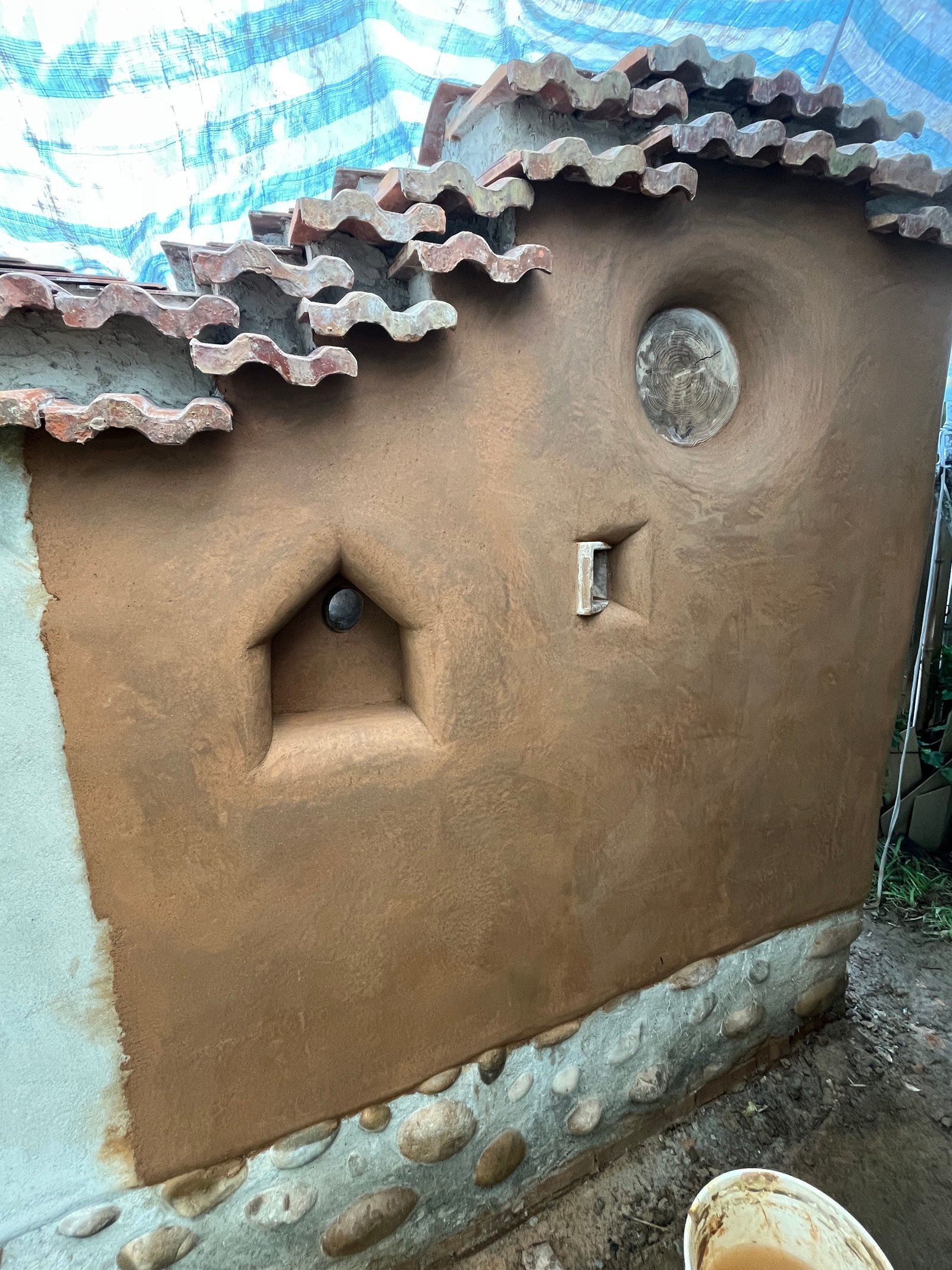 Lehmwand mit eingearbeiteten geometrischen Öffnungen und Wandnischen, Dachziegelabdeckung