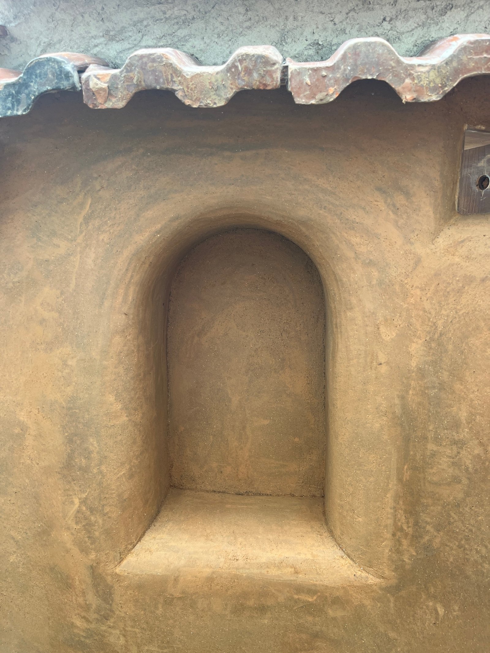 Lehmwandnische Detailansicht: gerundete Einbuchtung mit Lehmsockel und Dachziegel